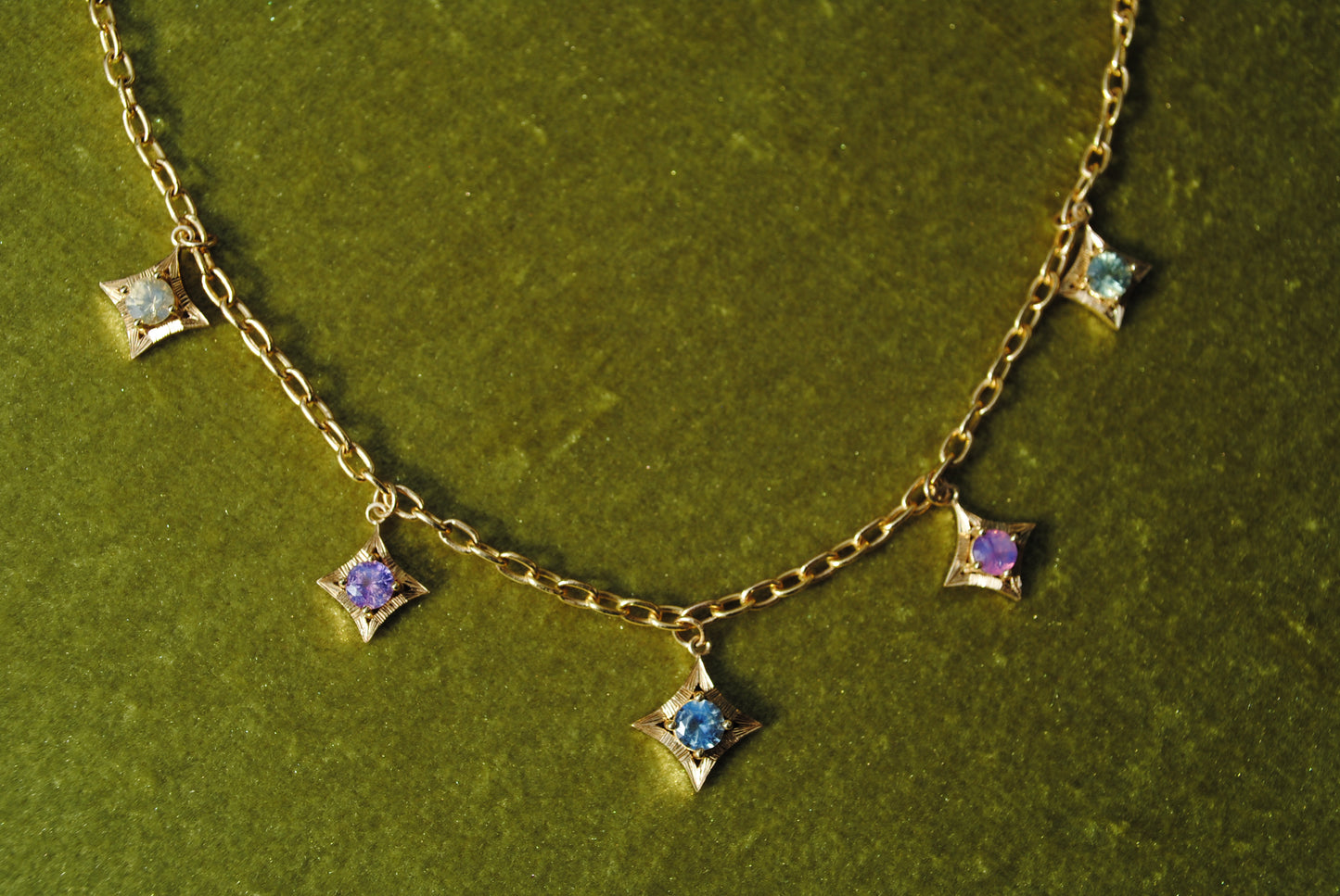 Gold necklace with star-shaped gemstones on a green textured background