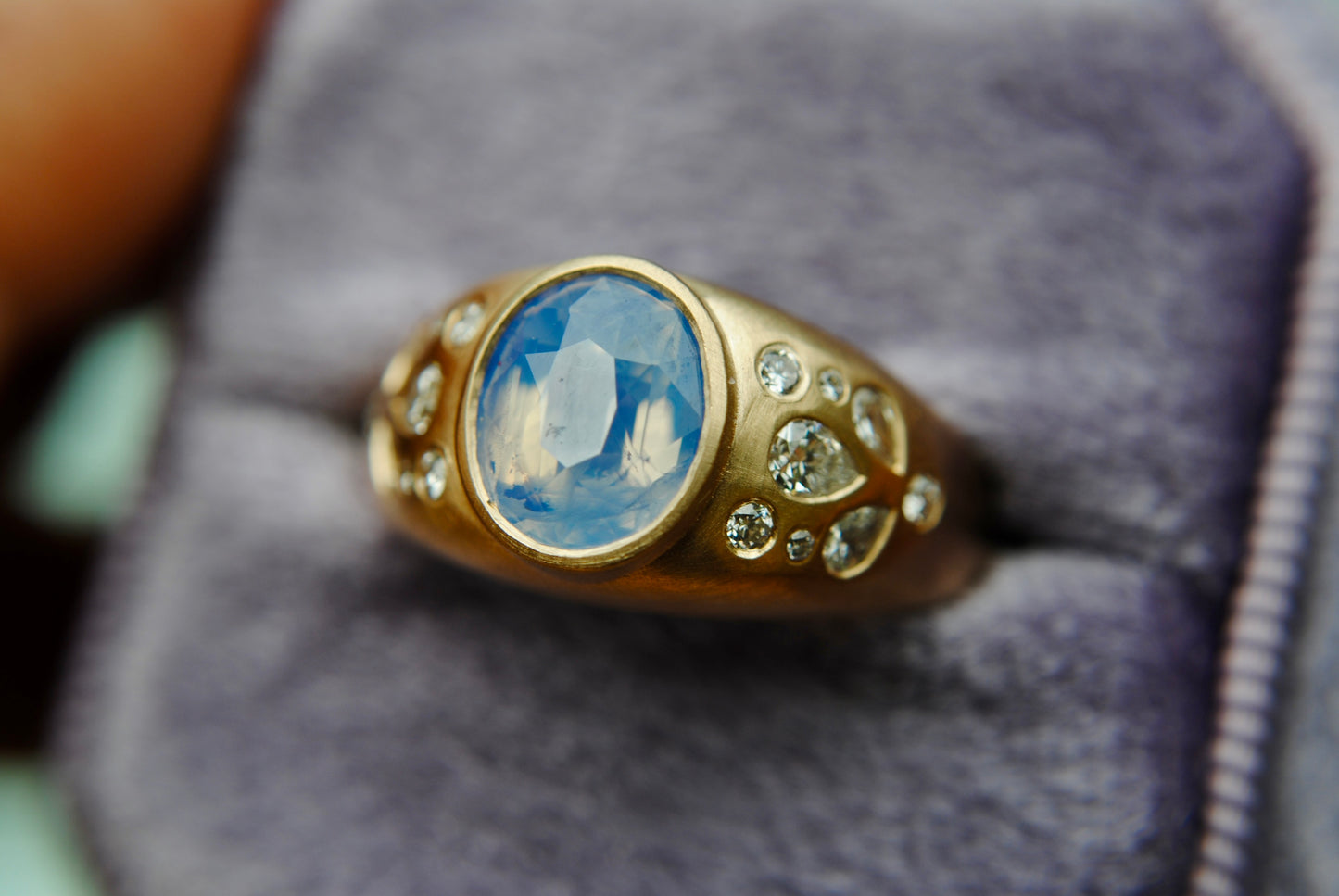 Ring with blue center stone and side diamonds against a blurred purple background