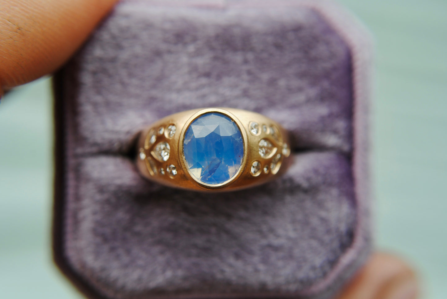 Ring with blue center stone and side diamonds against a blurred purple background