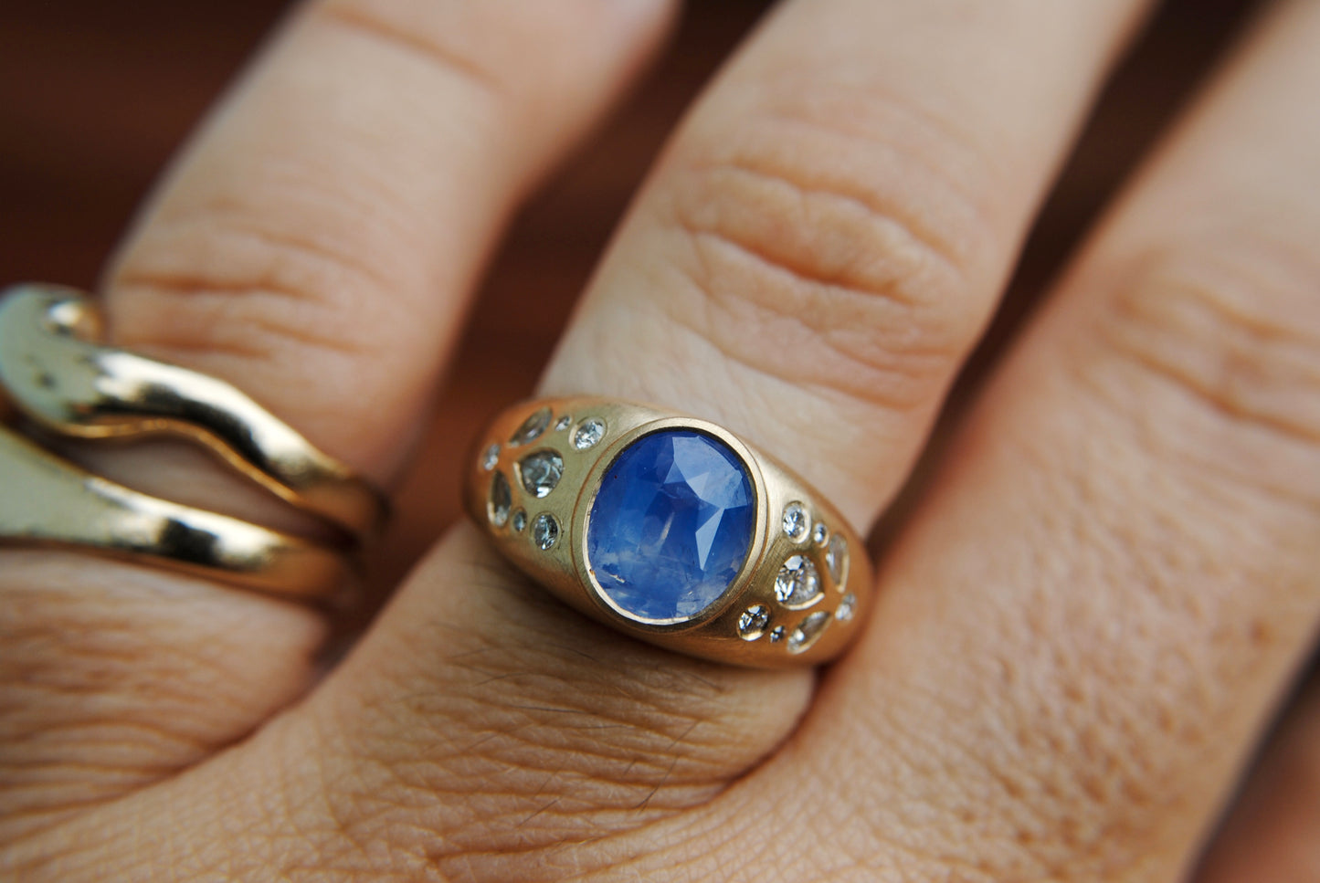 Ring with blue center stone and side diamonds shown on a hand