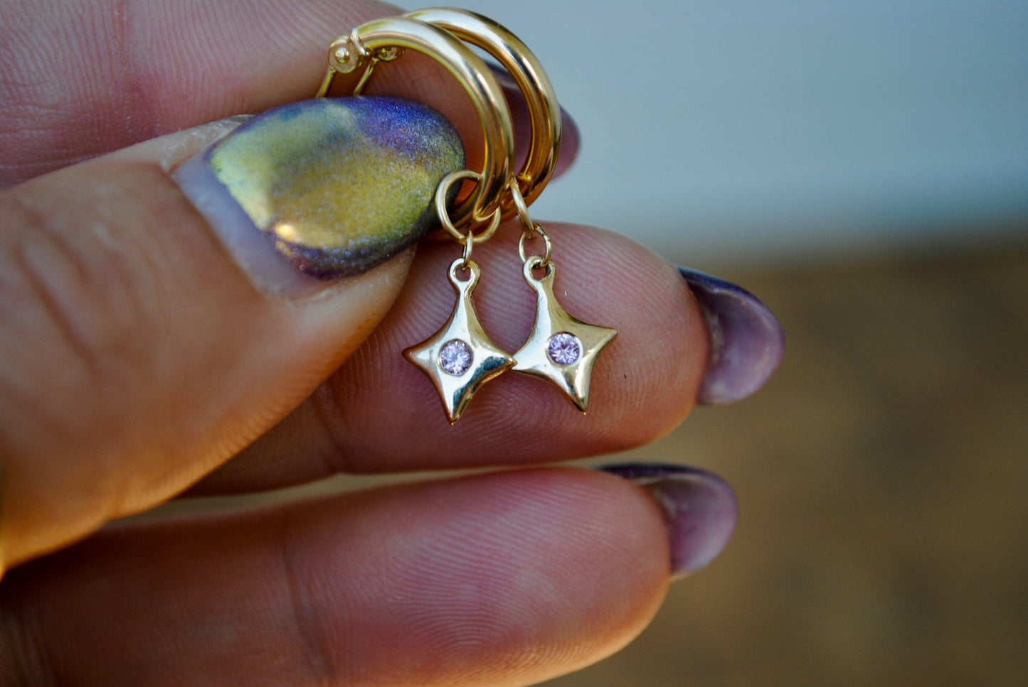 Gold earrings with star-shaped charms held between fingers
