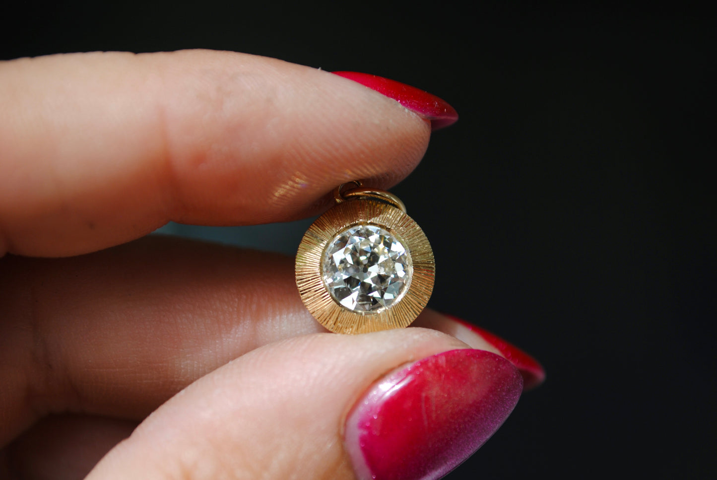 Gold earring with a diamond held between fingers against a dark background