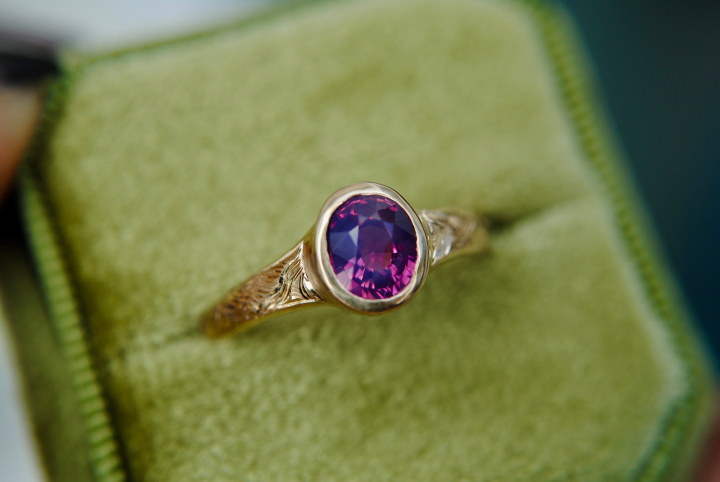 Gold ring with a purple gemstone on a green cushion