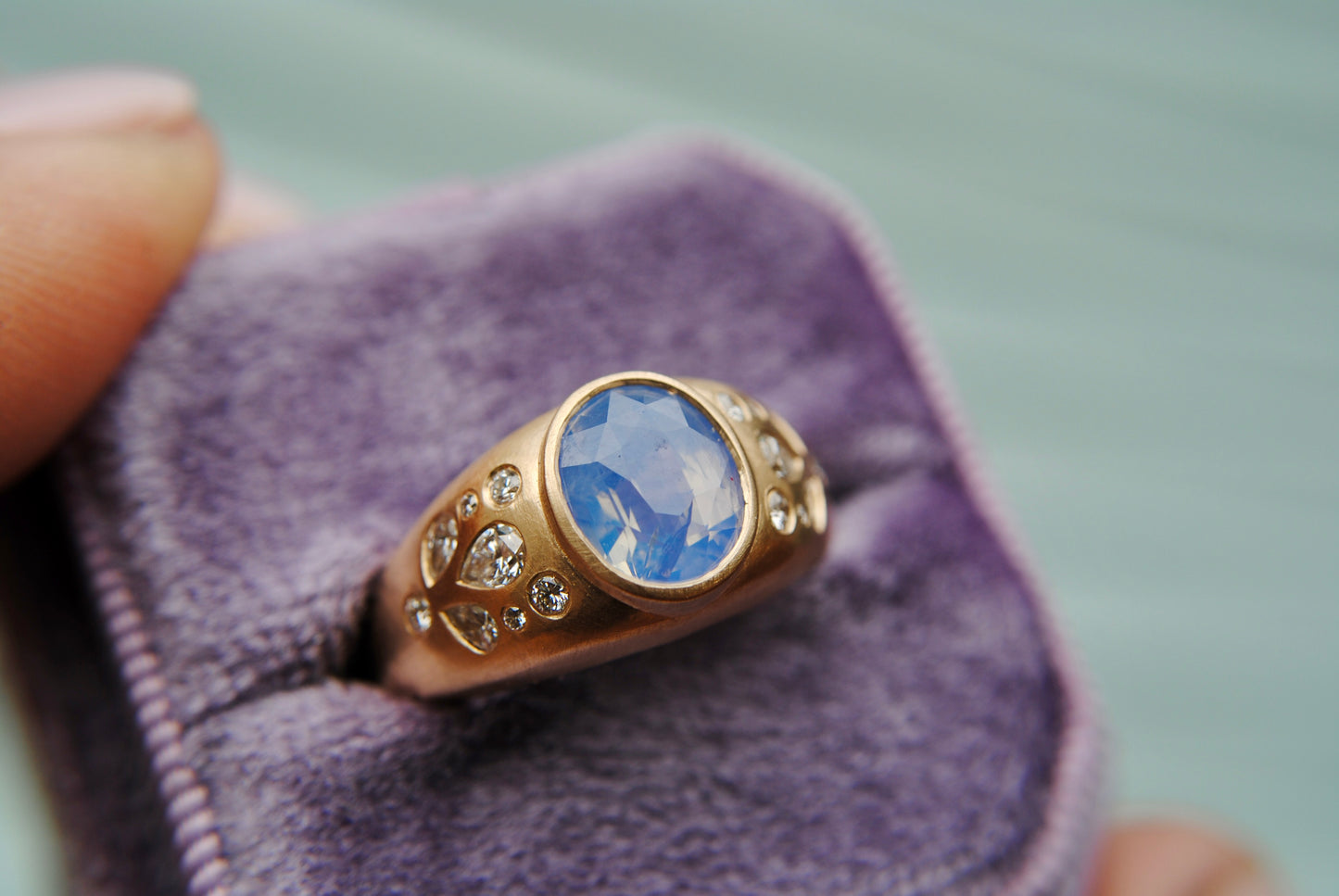 Ring with blue center stone and side diamonds against a blurred purple background