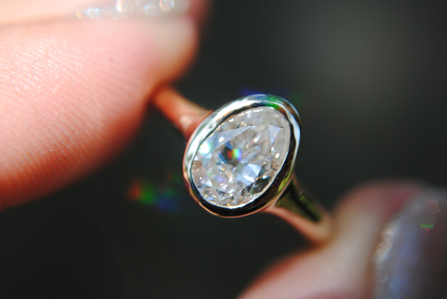 Close-up of a diamond ring held between fingers with a dark background