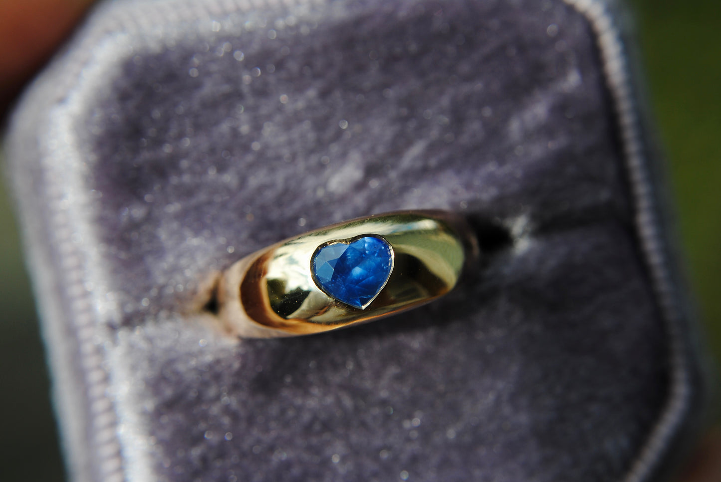 Gold ring with a heart-shaped blue gemstone on a gray background