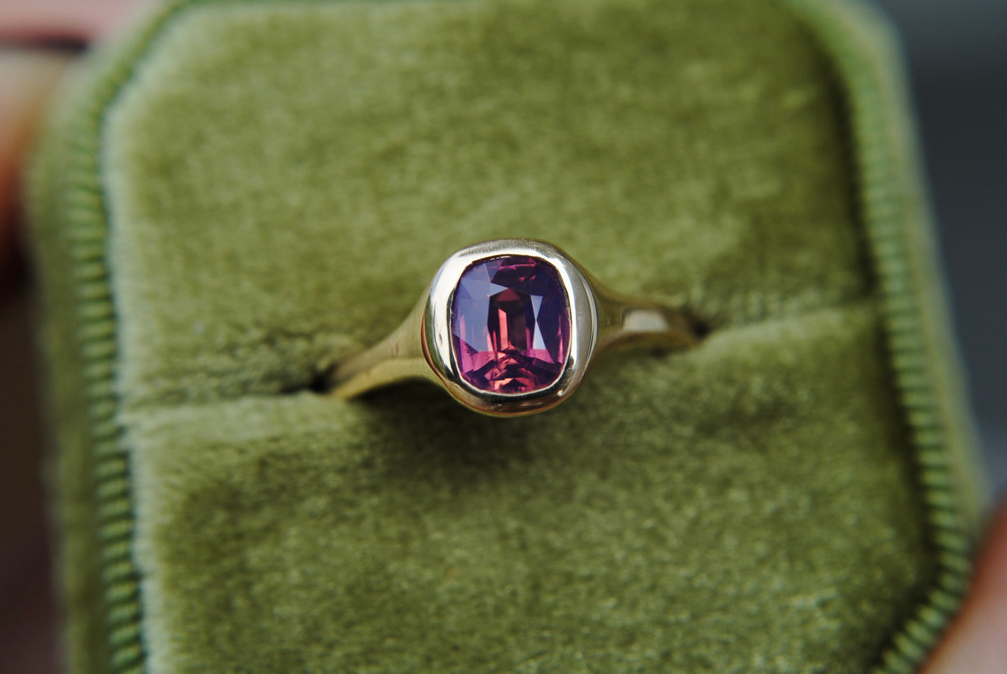 Gold ring with a purple gemstone on green velvet