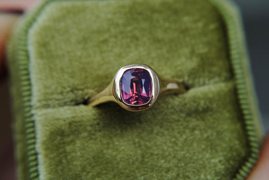 Gold ring with a purple gemstone on green velvet