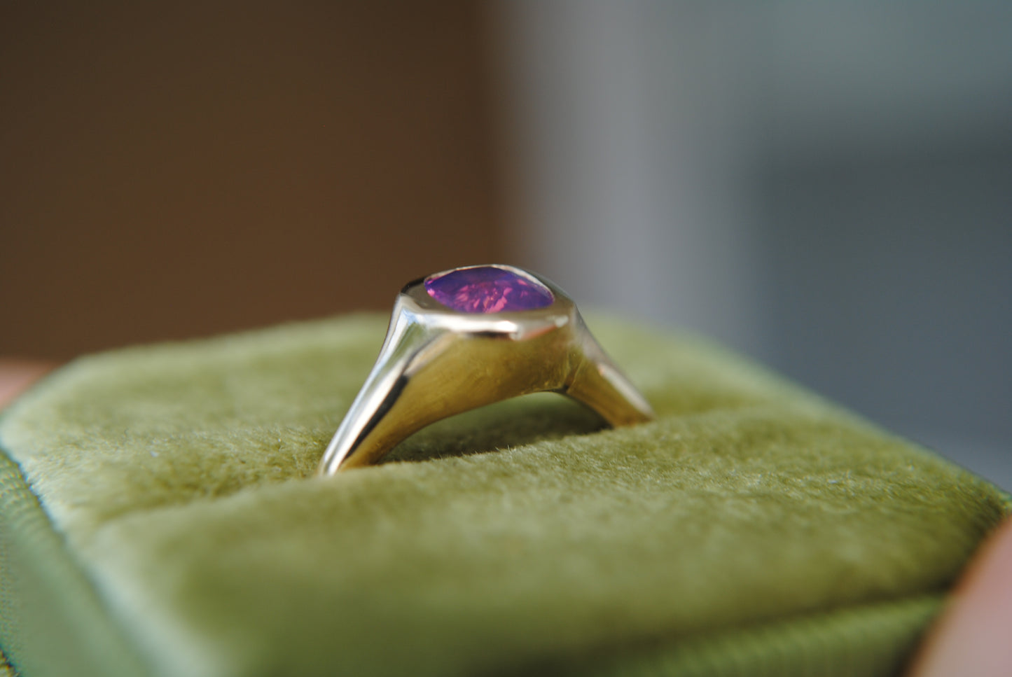 Gold ring with a purple gemstone on green cushion