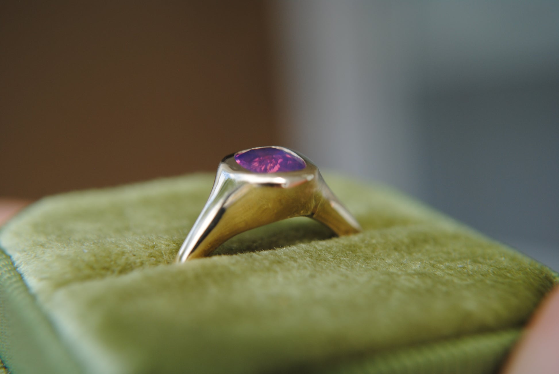 Gold ring with a purple gemstone on green cushion