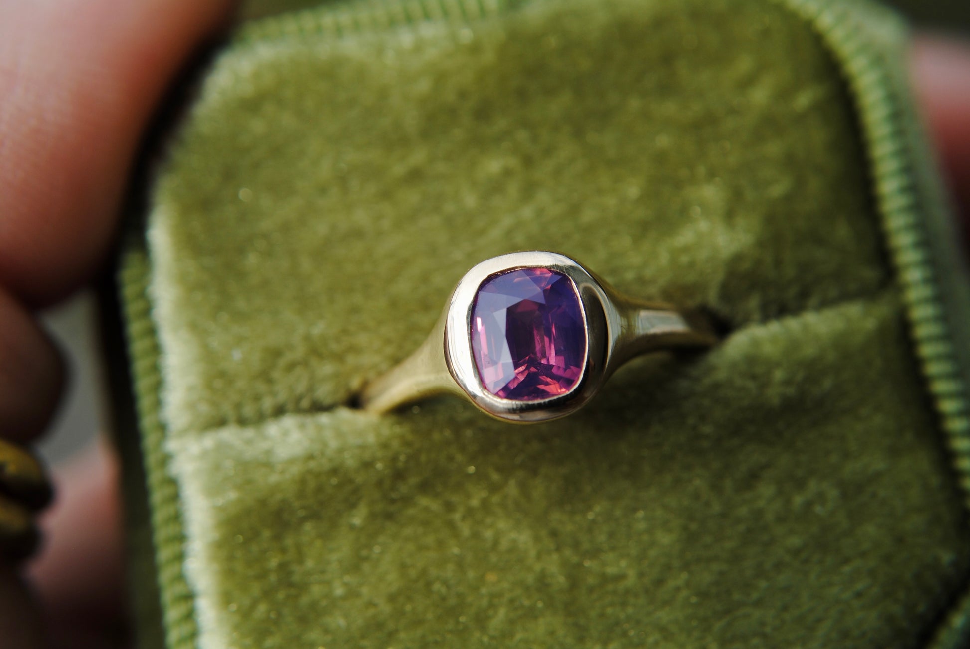 Gold ring with a purple gemstone on a green velvet cushion