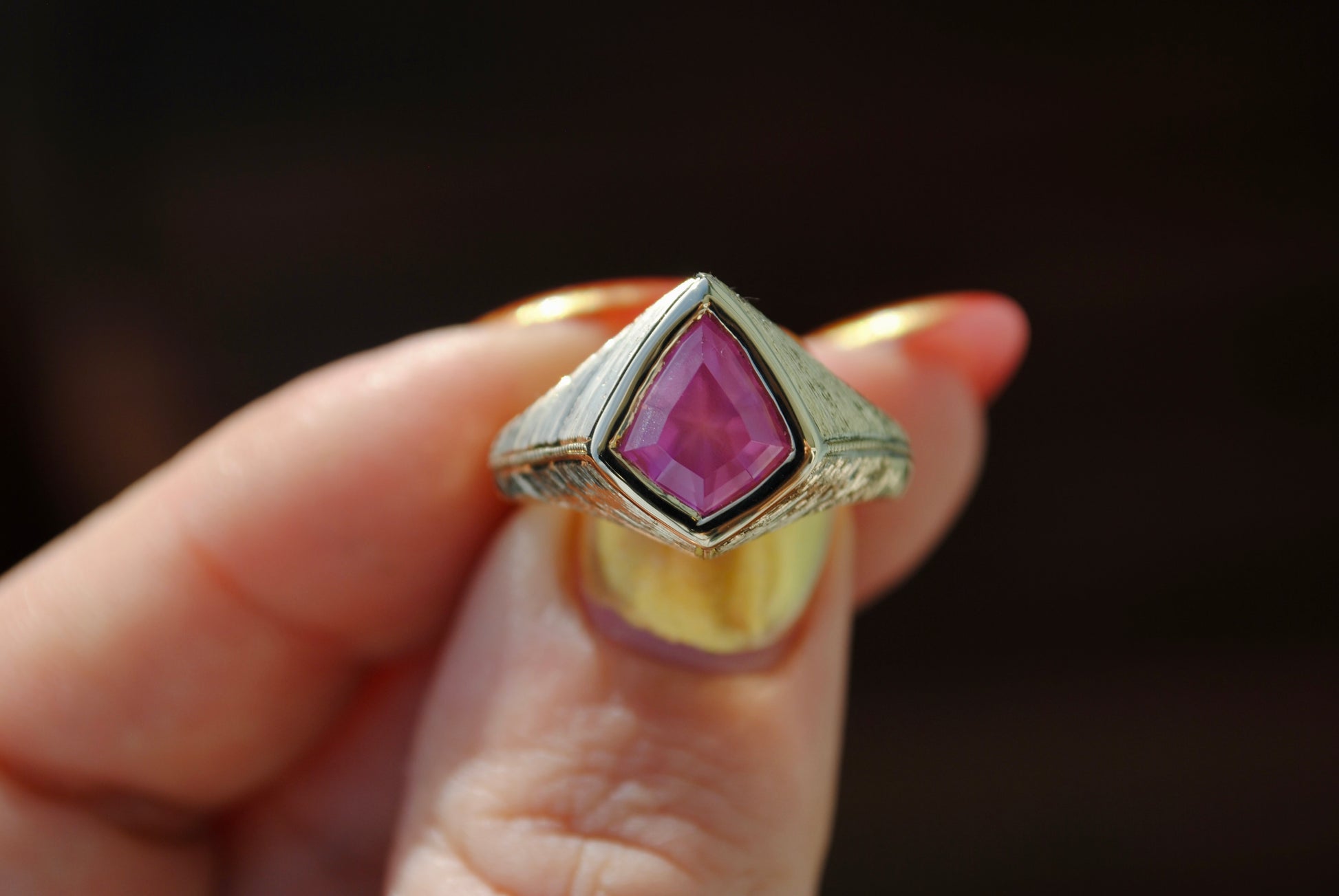 Gold ring with a pink gemstone held by a hand against a dark background