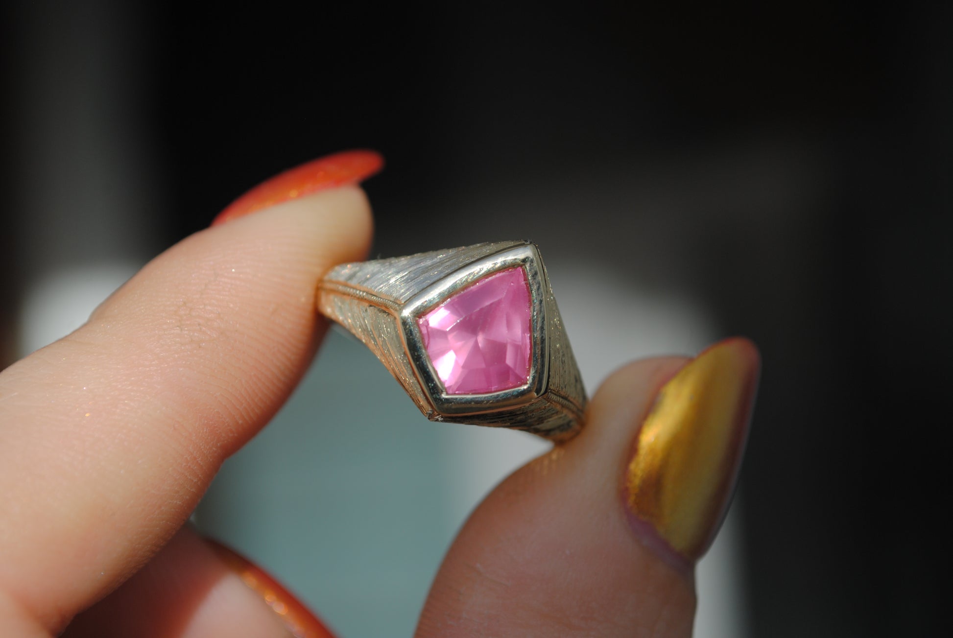Gold ring with a pink gemstone held by a hand against a blurred background