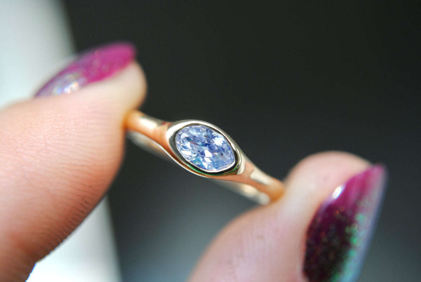 Gold ring with a blue gemstone held by a hand with purple nail polish.