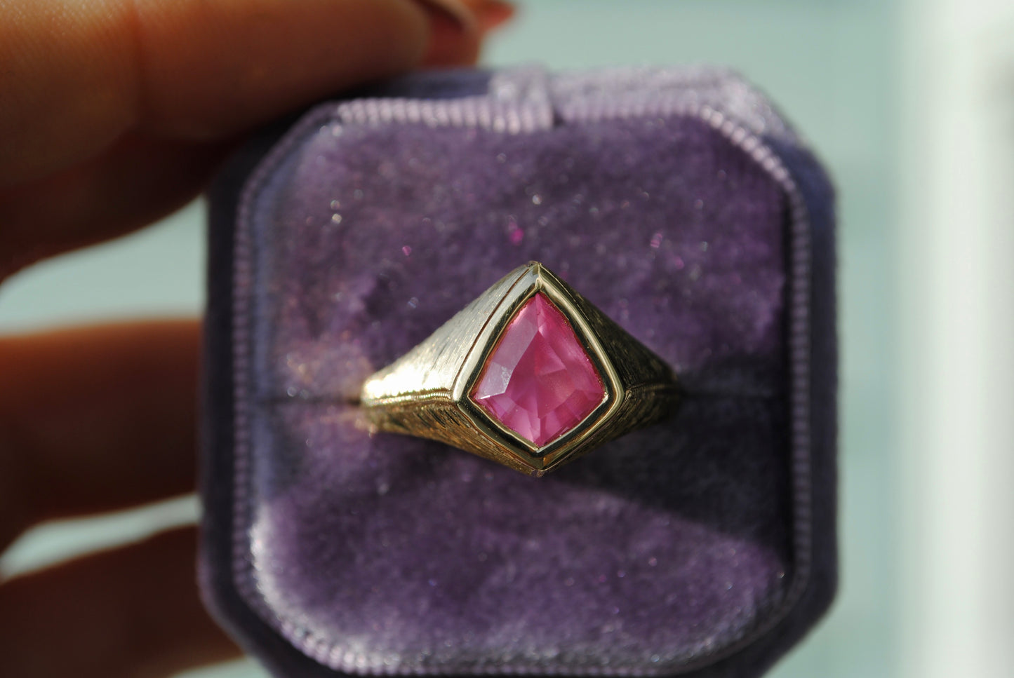 Gold ring with a pink gemstone on a purple cushion