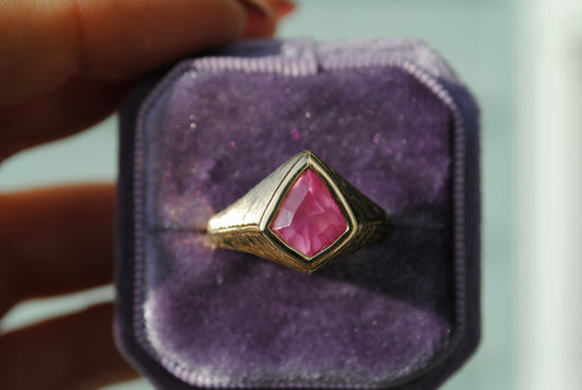 Gold ring with a pink gemstone on a purple cushion