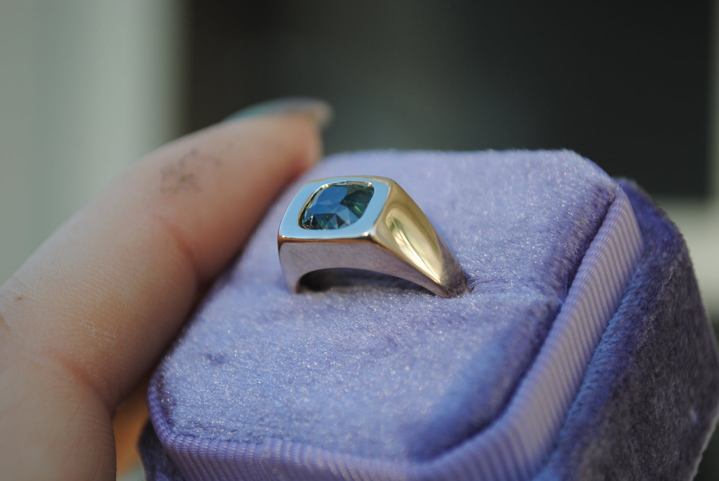 Gold and silver ring with a blue gemstone on a purple cushion