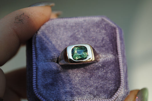 Ring with a green gemstone in a purple velvet box held by a hand.
