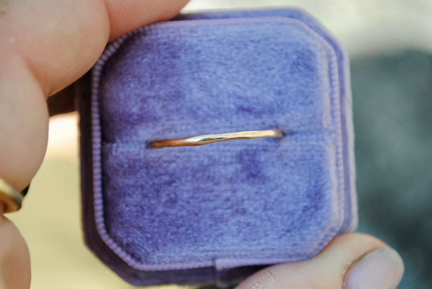 Gold ring in a purple velvet box held by a hand with a blurred background