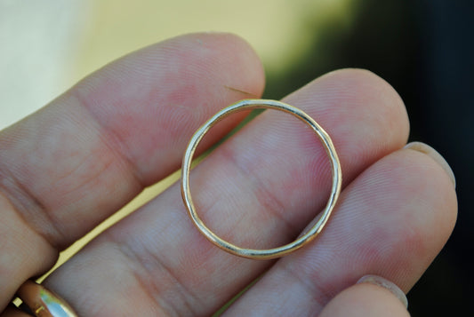 Gold ring held between fingers with a blurred background