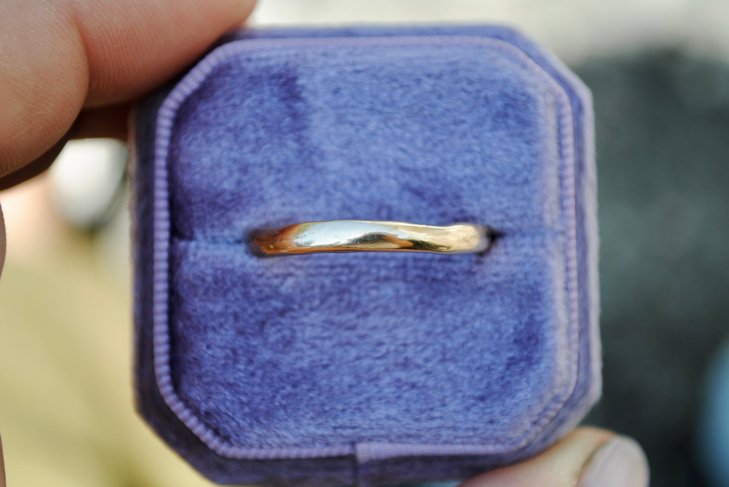 Gold ring in a purple jewelry box held by a hand
