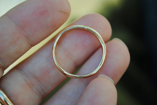 Gold ring held between fingers with a blurred background