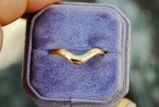 Gold ring in a purple jewelry box held by a hand with a blurred background