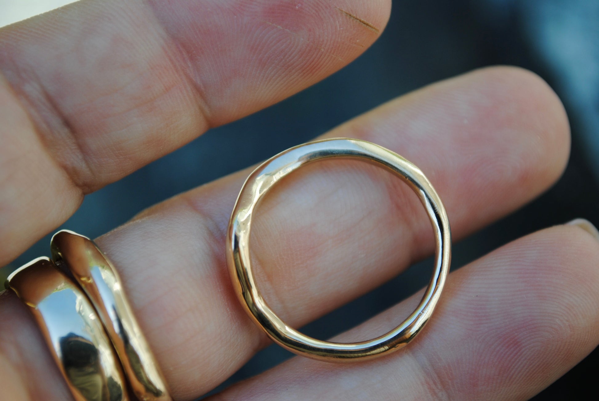 Gold ring held between fingers against a blurred background