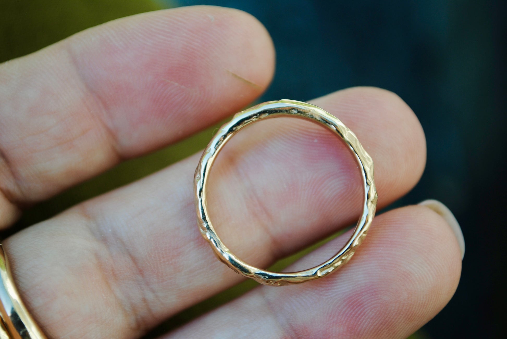 Gold ring held between fingers with a blurred background