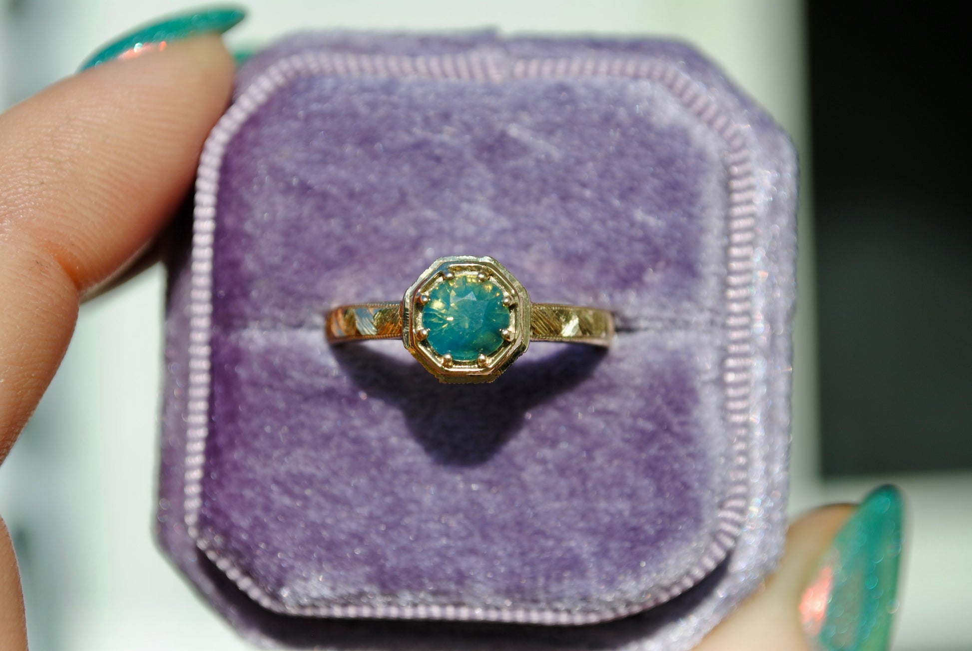 Gold ring with a green gemstone on a purple cushion
