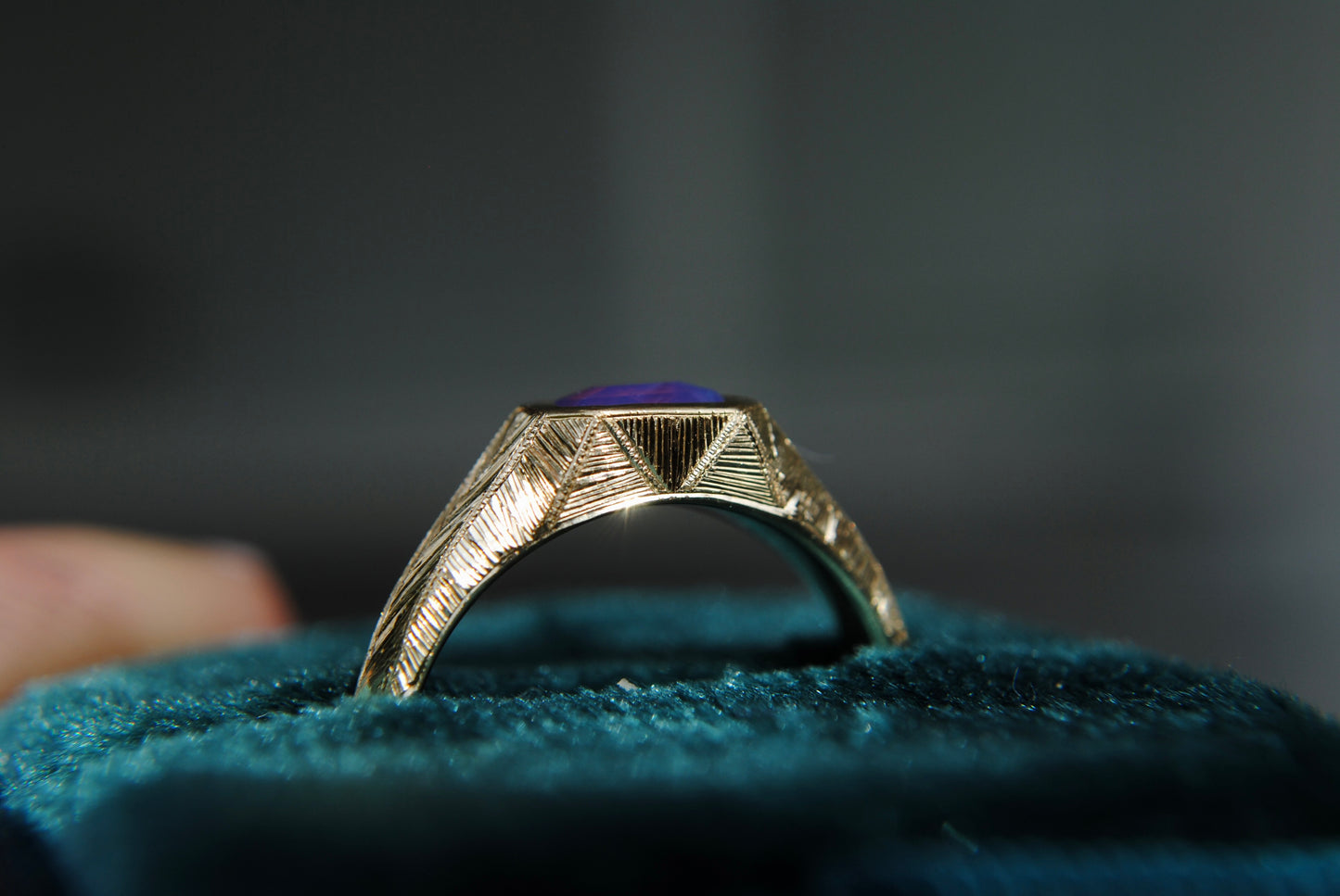 Gold ring with a purple stone on a textured blue surface