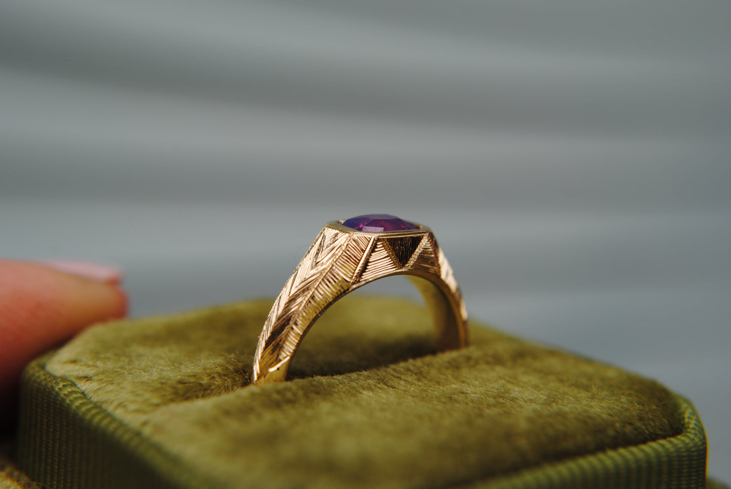 Gold ring with a purple gemstone on a green velvet cushion against a blurred background