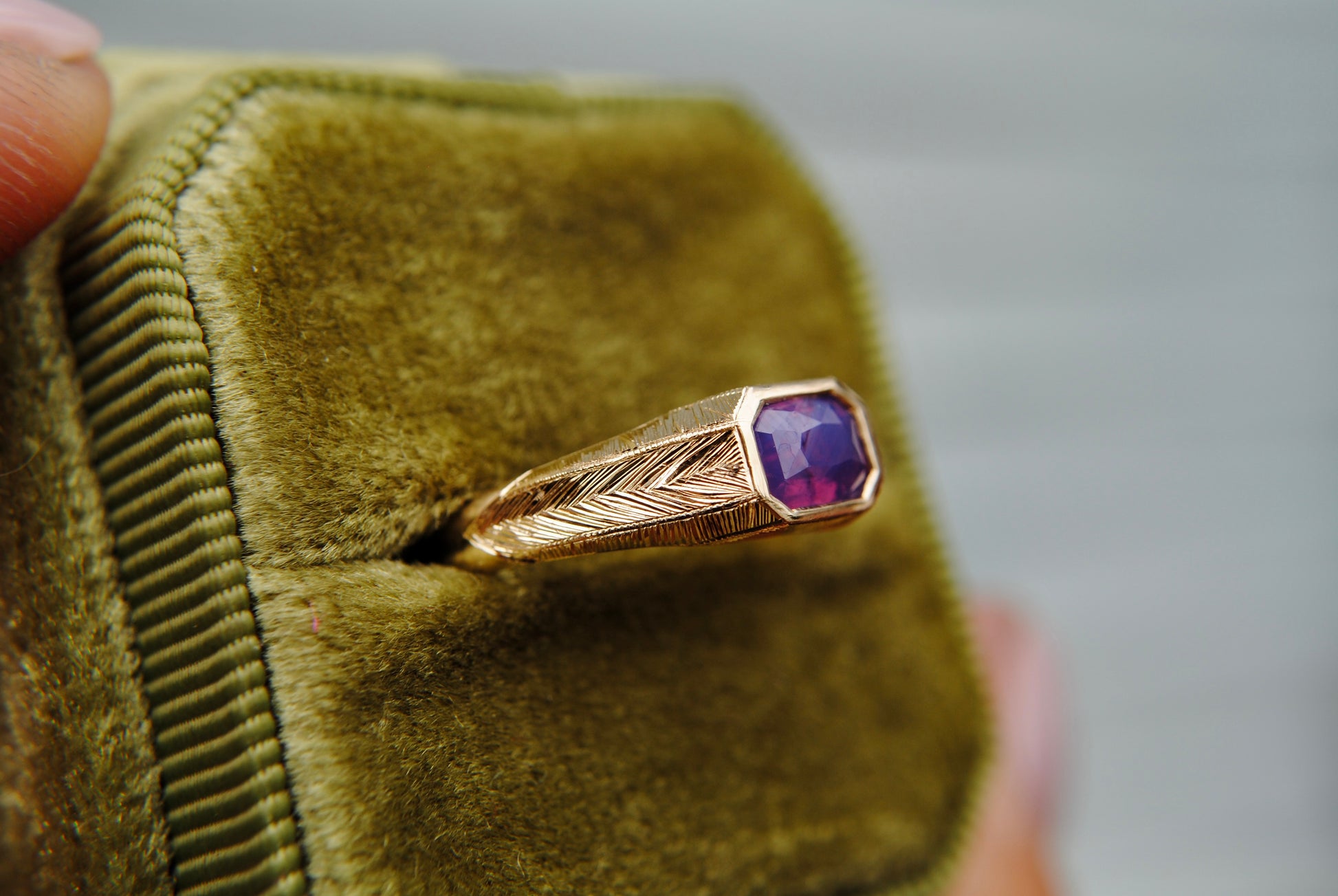 Gold ring with a purple gemstone on a green velvet cushion