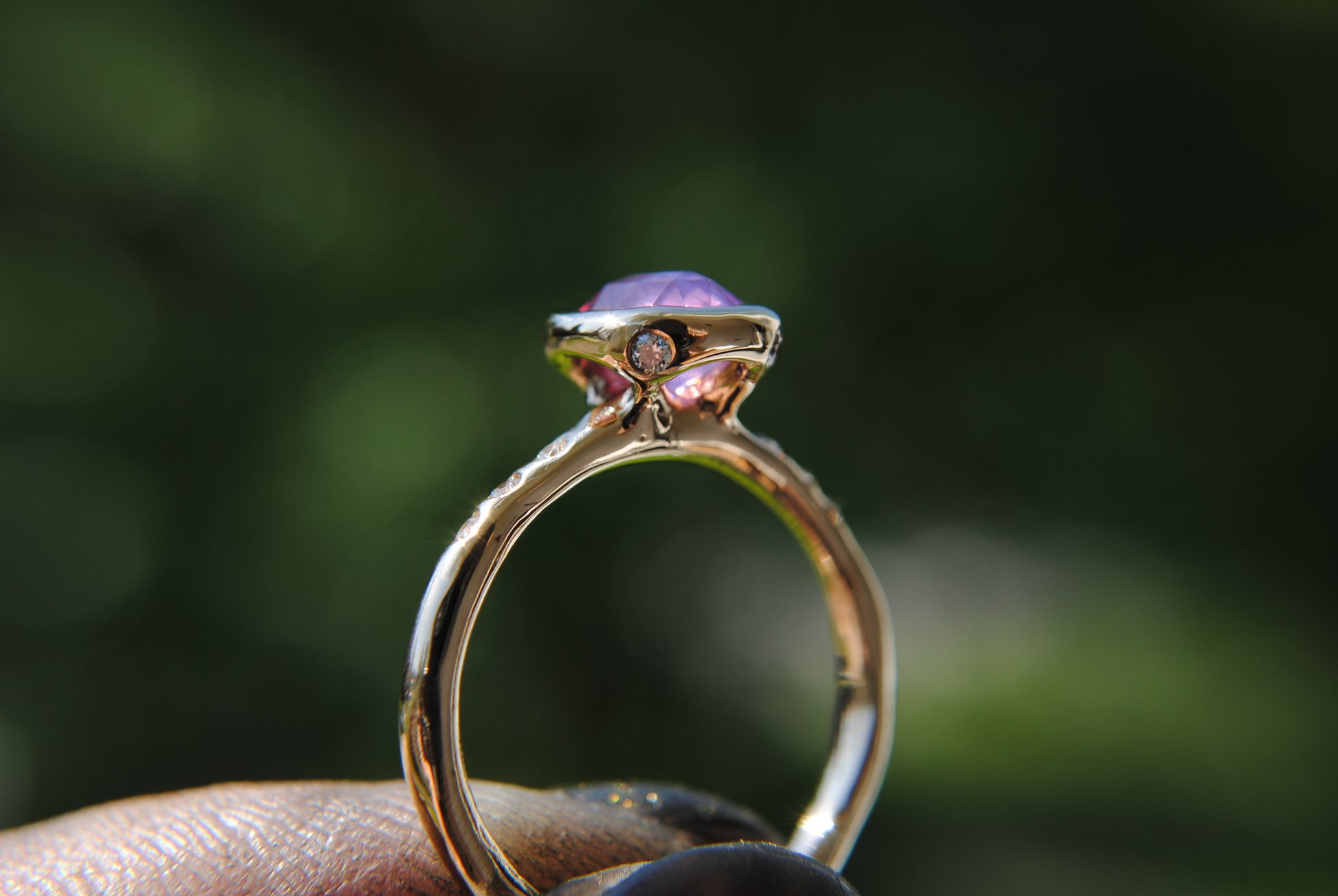 Gold ring with a purple gemstone held by a hand against a blurred green background