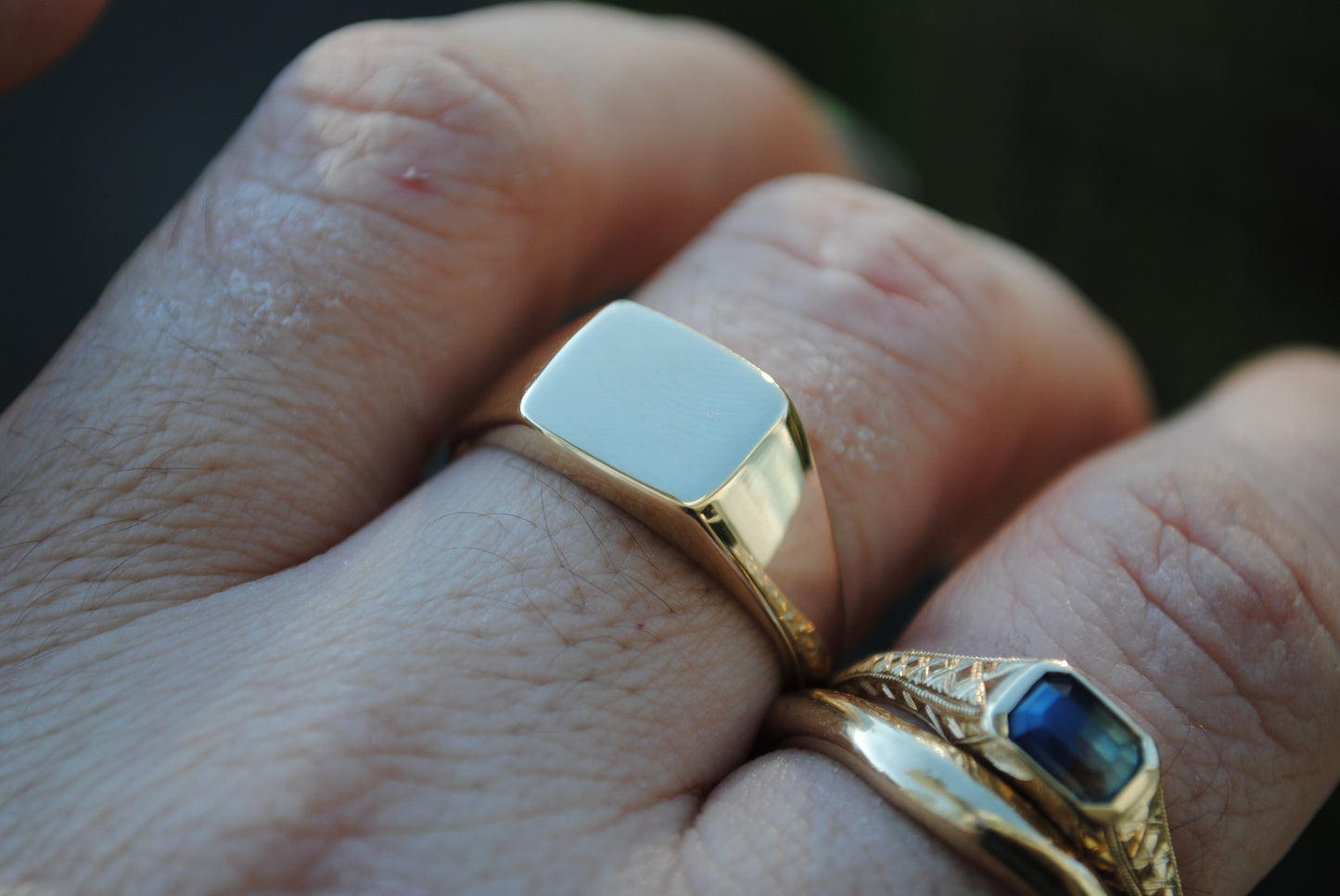 Close-up of a hand wearing two gold rings with a white stone and blue gemstone.