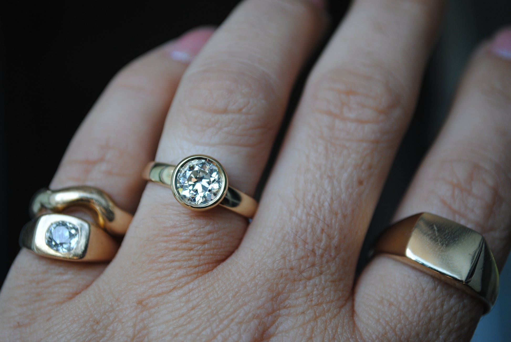 Close-up of a hand wearing two gold rings with diamond stones on a dark background