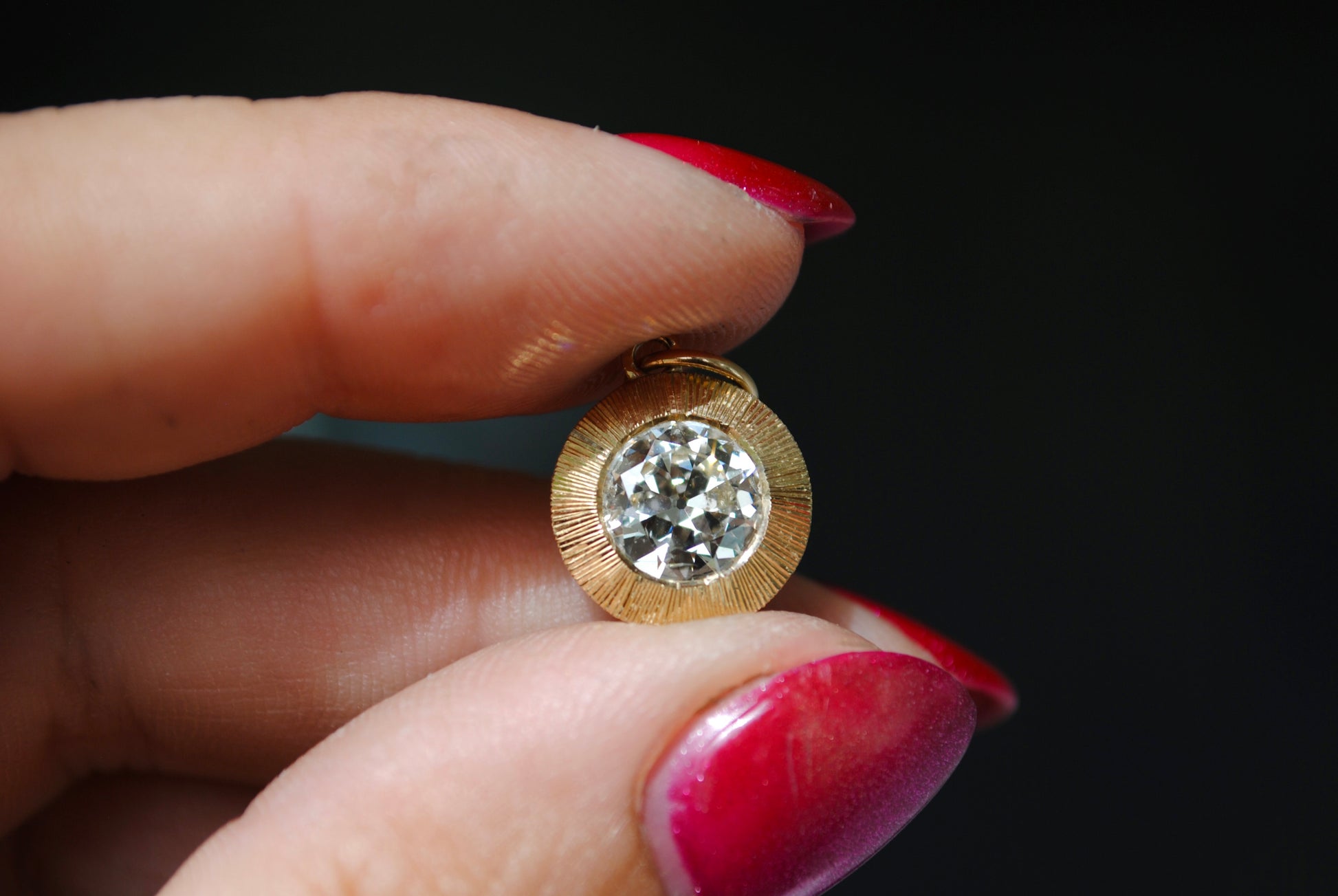 Gold earring with a diamond held between fingers against a dark background