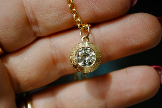 Gold necklace with a diamond pendant held in a hand