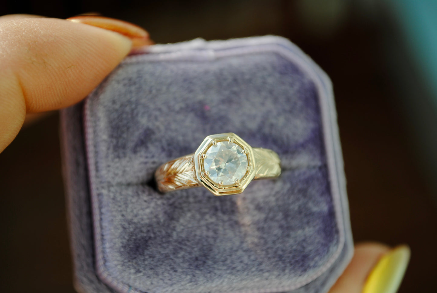 Gold ring with a diamond in a purple jewelry box held by a hand.