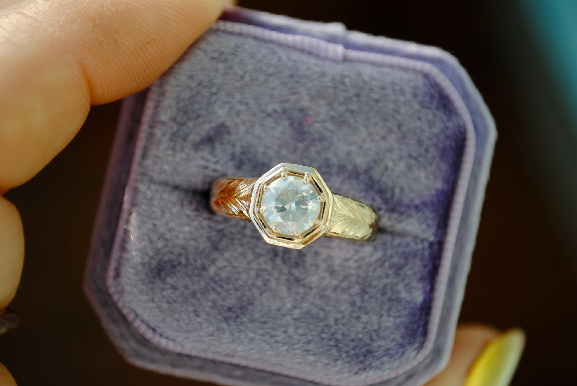 Gold ring with a diamond in a purple velvet box held by a hand.