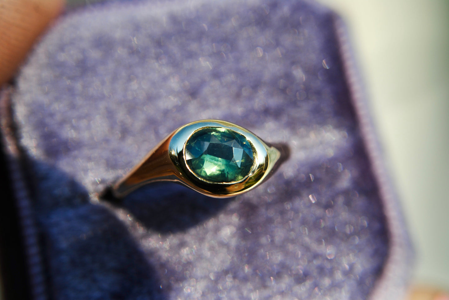 Gold ring with a green gemstone on a purple cushion