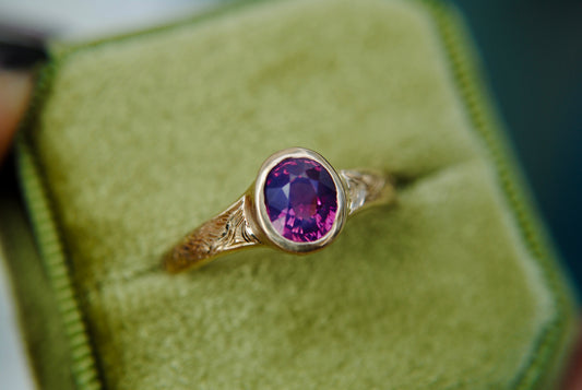 Gold ring with a purple gemstone on a green cushion
