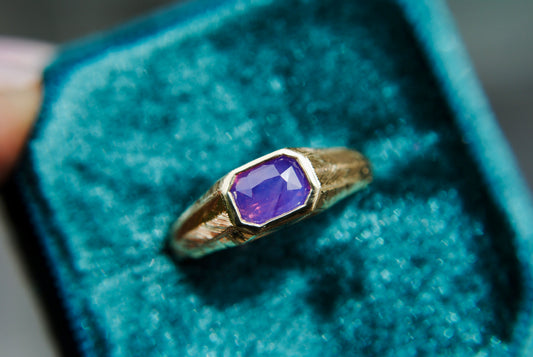 Gold ring with a purple gemstone on a blue textured background