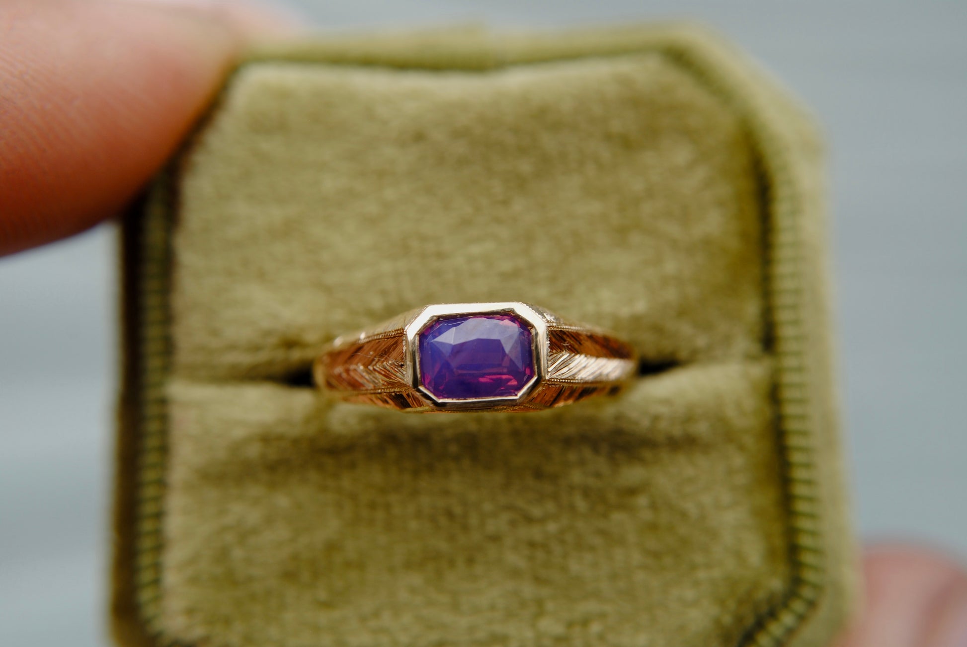Gold ring with a purple gemstone in a beige velvet box.