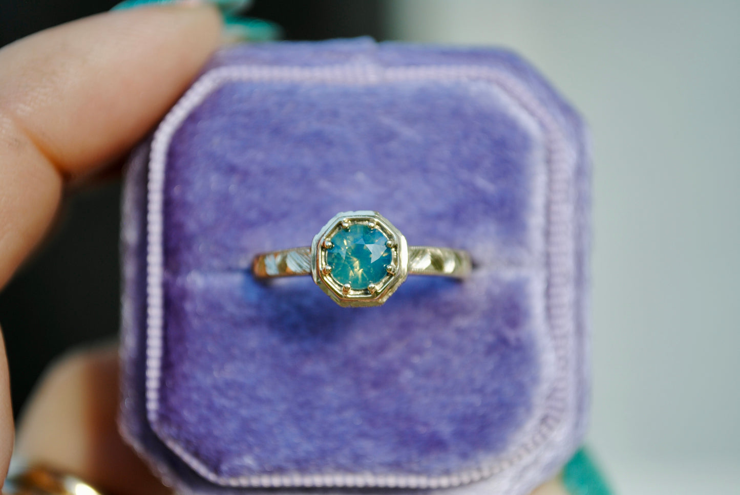 Gold ring with a blue gemstone in a purple jewelry box held by a hand.
