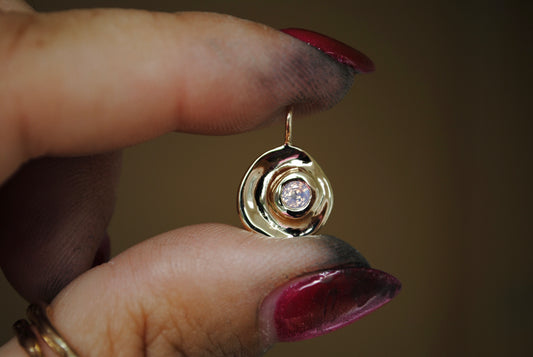 Gold earring with a diamond held between fingers against a blurred background