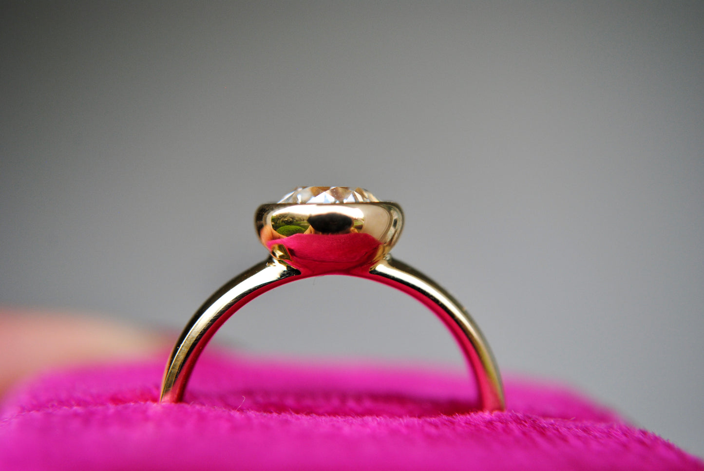 Gold ring on a pink cushion with a gray background