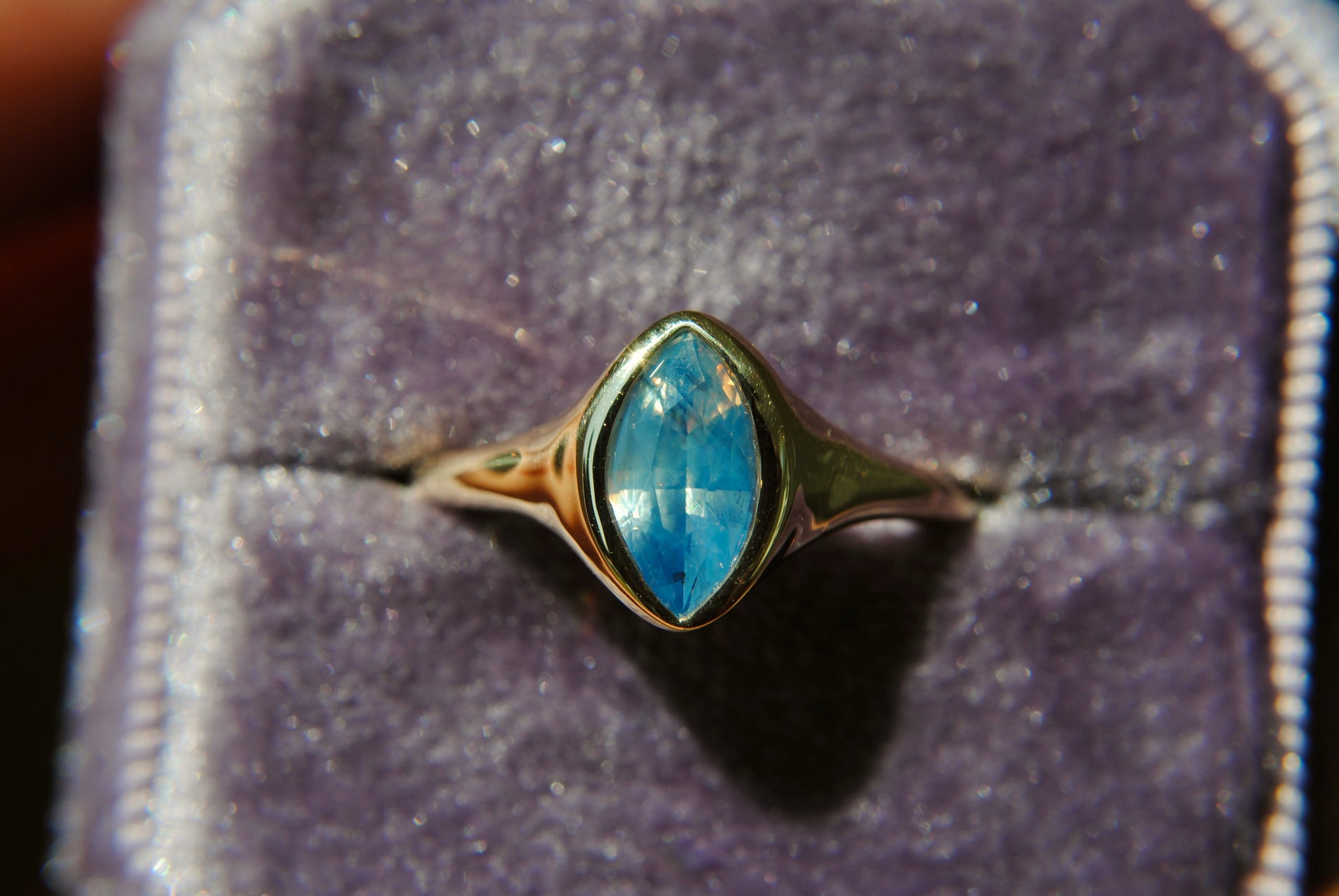 Ring with a blue gemstone in a gold setting on purple velvet