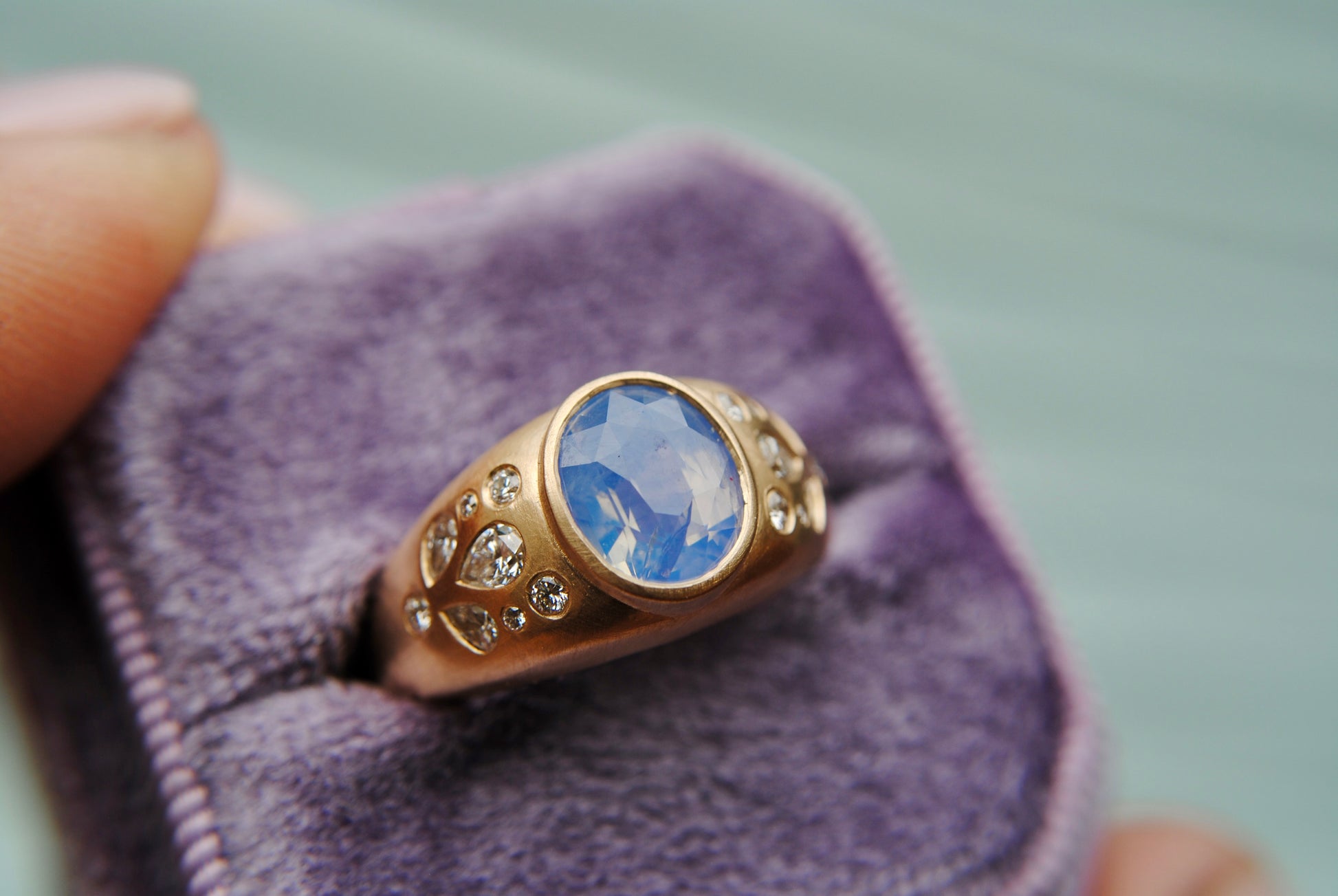 Ring with blue center stone and side diamonds against a blurred purple background
