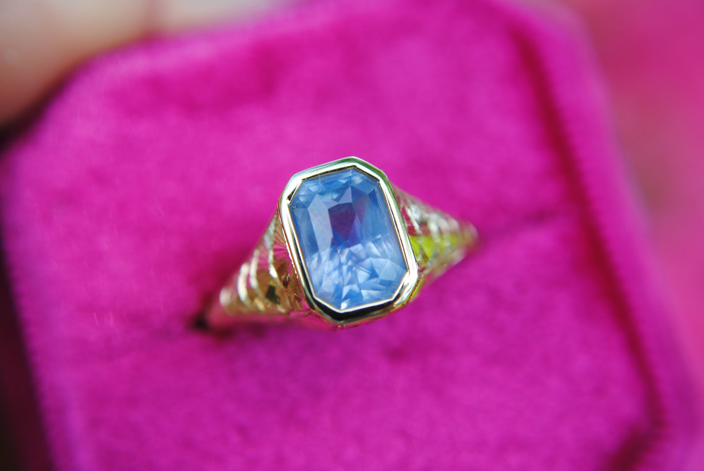 Gold ring with a blue gemstone on a pink background